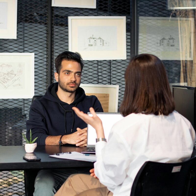 a man sitting at a desk talking to a woman
